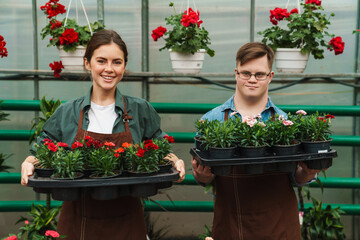 Man with down syndrome and woman smiling and holding plants while working in greenhouse