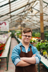Man with down syndrome smiling while standing in greenhouse with arms folded