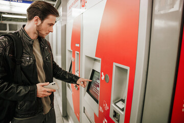 Young man using atm bank machine while standing in subway