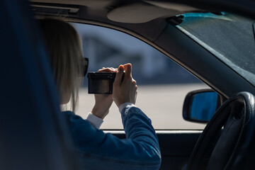 Woman in sunglasses with a camera sits in a car and takes pictures with a professional camera, a private detective or a paparazzi spy. Journalist is looking for sensations and follows celebrities. - obrazy, fototapety, plakaty