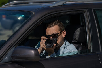 Man in sunglasses with camera sits inside car and takes pictures with professional camera, private...