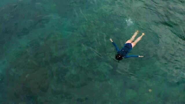 Top aerial view of female snorkeling and trying diving on water of ocean. Enjoy exploring sea and coral reef with snorkel and mask. Girl beginner amateur freediver swims breaststroke enjoying peace 