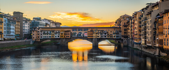 UNESCO site Ponte Vecchio in Florence early in the morning dawn with arched sun reflection.