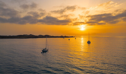 Fototapeta premium Dramatic warm sunrise low level aspect aerial image with silhouetted boats moored off the island of Lobos near Corralejo in Fuerteventura Canary Islands Spain