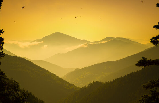 Silhouette of mountain range at sunset. Paragliders on the mountain. Foggy image in mountain range