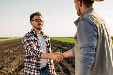 Two people shake hands in the field on a sunny day.