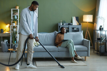 Fototapeta na wymiar Man vacuuming the floor with vacuum cleaner in the living room, he helping his wife to do housework