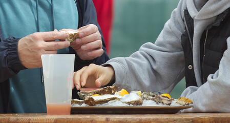 Eating oysters at a street food market, womens hands holding an oyster shell and a lemon over a tray of ice and other oysters.