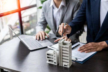 Real estate agents offer contracts to buy or rent housing. Businessman holding model small building...