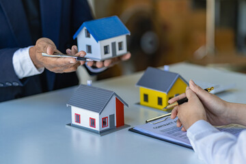 Real estate agents offer contracts to buy or rent housing. Businessman holding model small building house with property insurance at table in home sales office