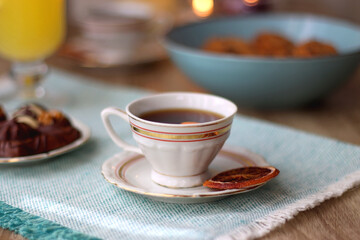 Plate of chocolate pralines, bowl of cookies, cups of tea, glasses of juice and lit candles on the table. Selective focus.