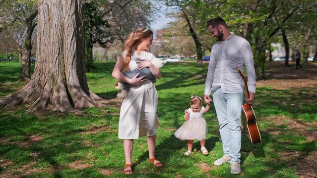 A married couple with 2 kids walking with a guitar at Cherry Blossom Park in Washington DC while holding their son and daughter