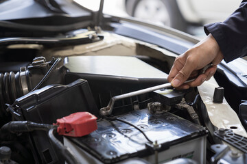 Car mechanic maintenance and auto service shop concept. Male car mechanic repair, fix car engine in auto repair shop. Technician inspecting quality parts of battery, electronic in garage workshop