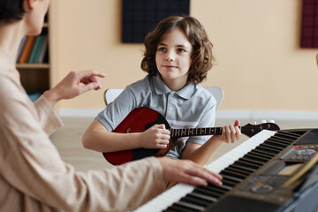 Young student playing balalaika with teacher conducting and playing piano in musical lesson