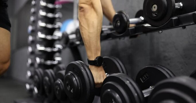 Male athlete with fitness watch on hand taking dumbbell for sports training in gym closeup 4k movie slow motion. Healthy lifestyle concept