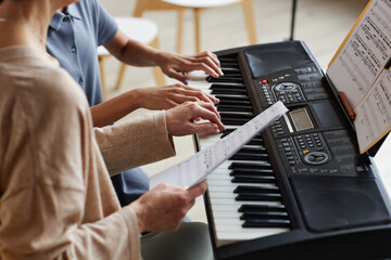 Close-up of girl learning to play piano together with teacher who using sheet music in music school © Seventyfour