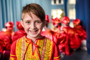 a boy dancer with his group in red-orange folk costumes are rehearsing the dance and waiting for...