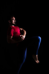 Fototapeta na wymiar hombre creando una pose de artes marciales con malla azul y camiseta deportiva roja. Fotografía de estudio. Aislado sobre fondo negro. Espacio para texto