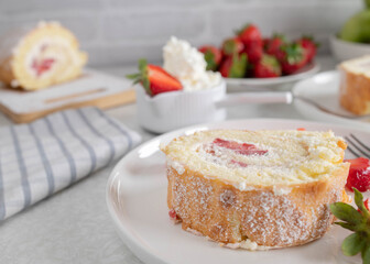 Slice of swiss roll with whipped cream and strawberry filling on a plate on light background