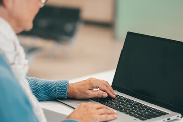 Defocused senior woman sitting at white desk using laptop. Mature caucasian lady typing on keyboard in business work