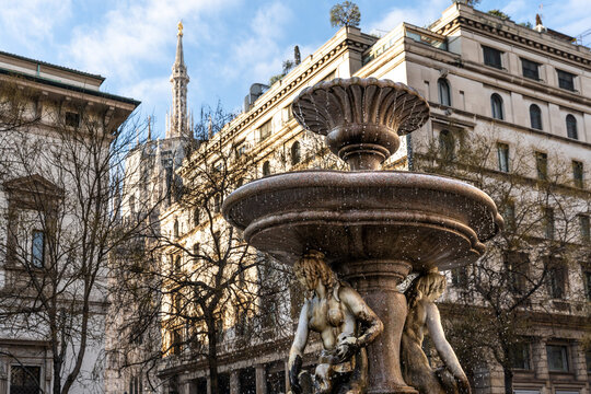 Marble fountain in piazza Fontana square erected in 18th century by sculptor Giuseppe Piermarini, with the spires of Milano cathedral in the background, Milan city center, Lombardy region, Italy