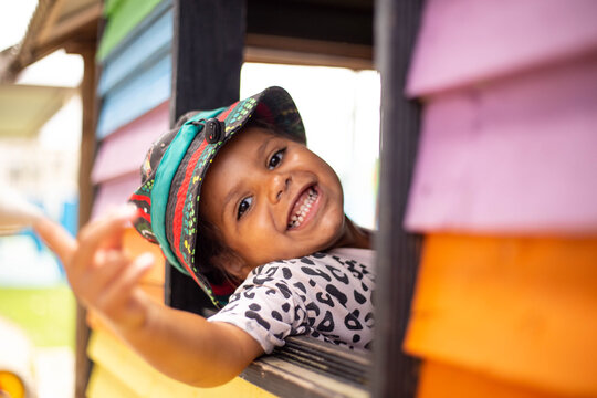 Young Aboriginal girl in a cubby house looking out window grinning