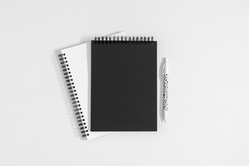 Flat lay top view of spiral blank black and white notepad mockup cover with pen isolated on white...