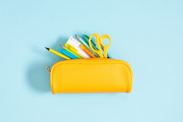 Back to school concept. Flat lay top view on yellow full pencil case with pencils and pens notepad scissors isolated on pastel blue background - obrazy, fototapety, plakaty