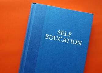 Blue text book on orange background with title text SELF EDUCATION - process of educating oneself...