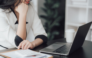Fototapeta premium Cheerful business lady working on laptop in office, Asian happy beautiful businesswoman in formal suit work in workplace. Attractive female employee office worker smile.
