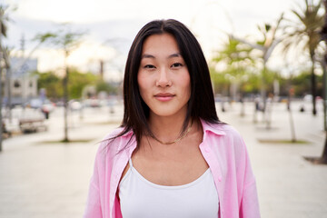 Portrait of Asian woman looking at camera carefree, standing outdoors in a beach city for summer trip.
