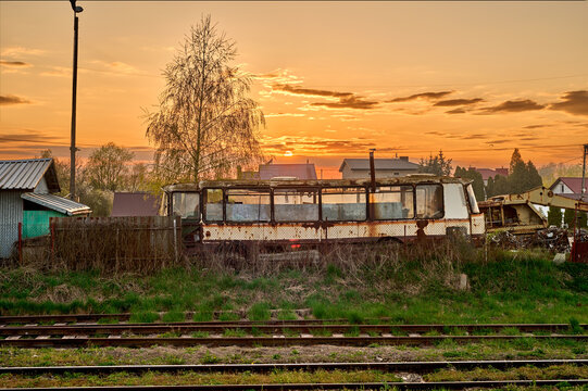 Rusty old dilapidated bus by the track against the red evening sky
