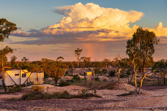 Rain falling from a large thunderstorm over an outback mining landscape at sunset