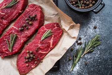 Fresh meat. Raw beef steaks with rosemary and spices on parchment paper on a stylish board. Flat top view.