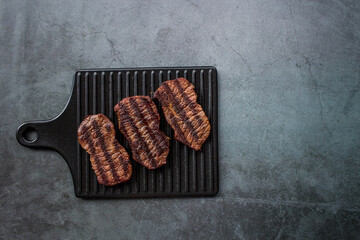 Fresh meat. Grilled beef steaks on a stylish board on a dark background. Flat top view.