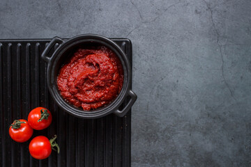 Tomato paste in a stylish black sauce pan on a ceramic dish. Preparation of seasoning, sauce. Canning vegetables.