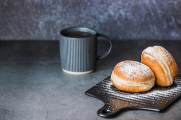 Delicious dessert. A doughnut with berry filling, fresh currant berries, powdered sugar and a cup of black coffee or tea on a dark background. Sweets.