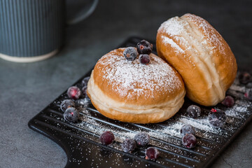 Delicious dessert. A doughnut with berry filling, fresh currant berries, powdered sugar and a cup of black coffee or tea on a dark background. Sweets.