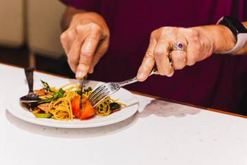 Woman eats Italian pasta with tomato using knife and fork.