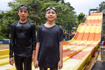 Two teenage boys wearing swimwear standing and smiling against the water slides