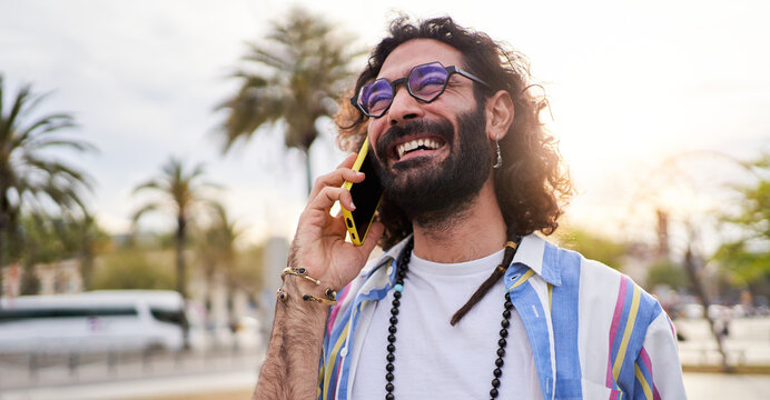 Fototapeta Happy hipster man speaking on the smartphone while walking outside in the street. Young male freelancer working from beach summer holidays. Copy space.