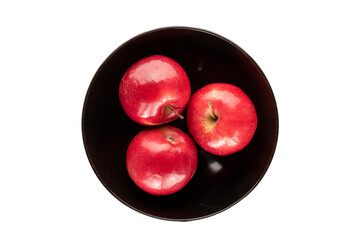 Three red apples in a black ceramic plate on a white background, top view.