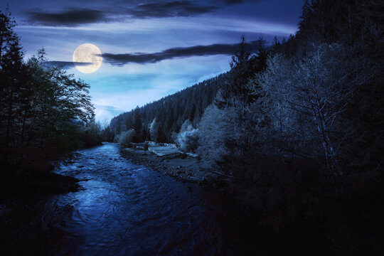 nature scenery with mountain river at night. green environment background with stones on the shore and forested hills in full moon light