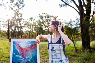 Happy young lady artist with paintbrush tucking hair behind ear