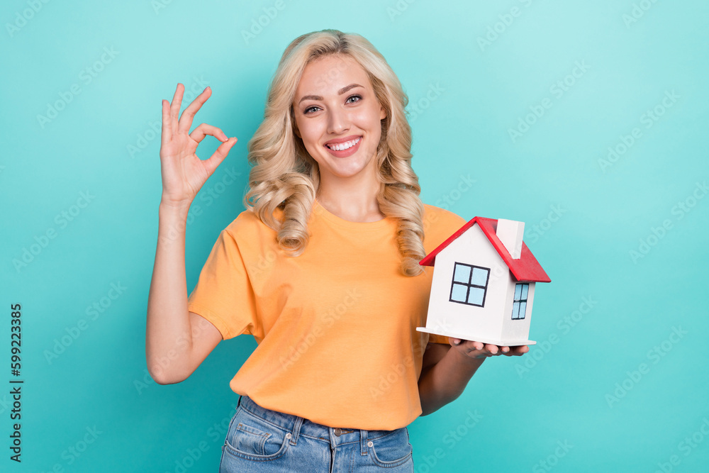 Sticker photo of charming confident girl wear orange t-shirt holding small house showing okey isolated turqu