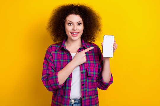 Photo of beautiful funny young woman chevelure hairstyle indicate finger phone interface ecommerce offer isolated on yellow color background - Powered by Adobe