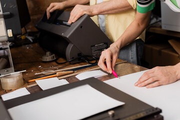 cropped view of typographer cutting paper with knife near colleague in print center.