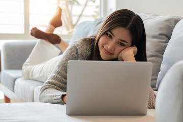 Smiling woman watching video using laptop, relaxing on a couch at home in the living room