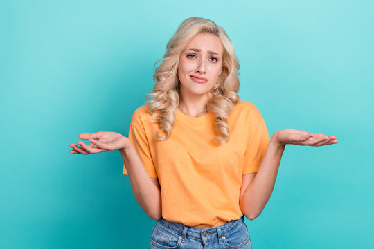 Photo of doubtful unsure girl wear orange t-shirt shrugging shoulders isolated turquoise color background