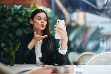 Stylish woman blogger tourist sits in a cafe with a phone in her hands reads a message, mobile communication and internet on a journey, video call, freelance work online, smile with teeth